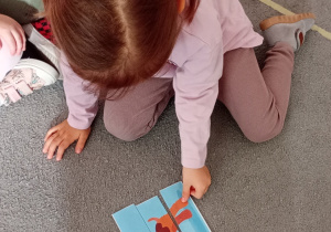 Dziewczynka w dwóch kitach układa puzzle przedstawiające psa.