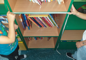 Dzieci z grupy Motylki mierzą szerokość półki z książkami.