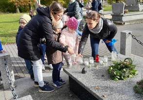 Dziewczynka i chłopiec z pomocą nauczycielek zapalają znicza