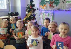 Na zdjęciu dzieci z grupy Liski stoją przy choince prezentując wykonane przez siebie laurki dla starszej Pani.