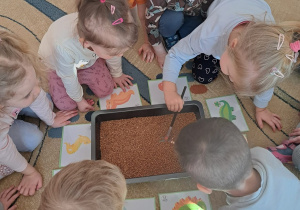 Dzieci z grupy Biedronki odnajdują za pomocą pędzelka ukryte szkielety dinozaurów.