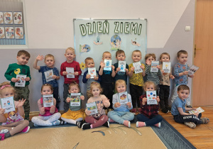 Dzieci z grupy Biedronki pozują do zdjęcia na tle tablicy z napisem Dzień Ziemi.