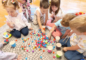 Dzieci bawią się kolorowymi kropkami – małymi pomponami. Segregują je do kolorowych kubeczków.