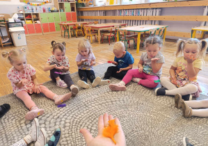 Dzieci siedzą w kole i bawią się kolorowymi piórkami.