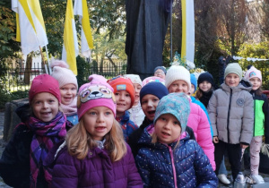 Dzieci z grupy Odkrywcy stoją przed pomnikiem Jana Pawła II.