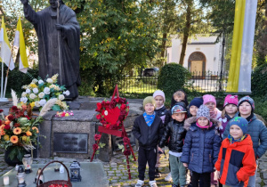 Dzieci z grupy Tropiciele pozują do wspólnego zdjęcia pod pomnikiem Jana Pawła II.