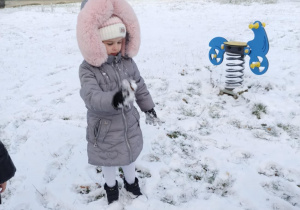 Dziewczynka z grupy Słoneczka rzuca kulkę ze śniegu.