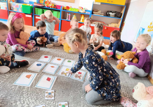 Dziewczynka układa obrazki przedstawiające Misia z odpowiednimi symbolami ćwicząc rozpoznawanie kształtu i koloru.