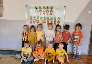 Dzieci z grupy Biedronki ubrane na pomarańczowo pozują do wspólnej fotografii z okazji „Dnia marchewki”