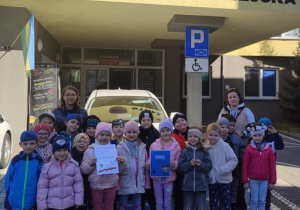 Dzieci z grupy Pszczółki pozują do zdjęcia przed budynkiem Straży Miejskiej.