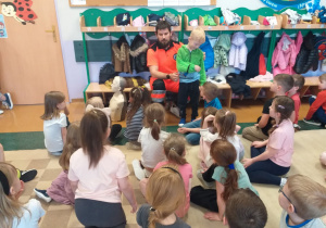 Ratownik medyczny pokazuje dzieciom jak można zabezpieczyć i unieruchomić górną kończynę.