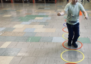 Chłopiec przeskakuje obunóż z obręczy do obręczy.