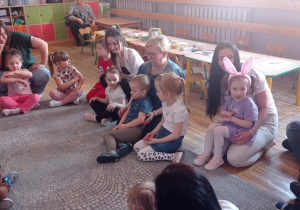 Dzieci siedzą w kole razem ze swoimi rodzicami.