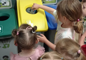 Zdjęcie przedstawia dziewczynkę wrzucającą plastikową butelkę do żółtego kosza.