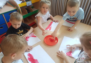 Dzieci z grupy „Słoneczka” malują paluszkami biało – czerwoną flagę.