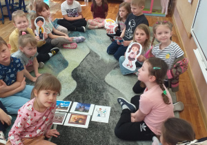 Dzieci z grupy Smerfy pozują do zdjęcia z obrazkami tematu „Zwiedzanie miasta” z kukiełkami.