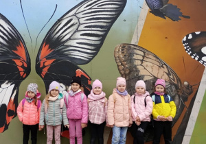 Dziewczynki z grupy Tropiciel pozują do zdjęcia na tle muralu z motylami.