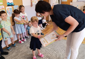 Nauczyciel wręcza dziewczynce pamiątkowy dyplom i upominek.