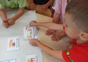 Chłopiec z grupy „Misie” nakleja obrazek, który mówi o tym, że należy pomagać innym.