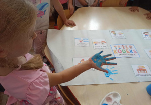 Dziewczynka z grupy „Misie” pokazuje pomalowaną na niebiesko rękę , którą odbije na kodeksie dobrego zachowania.