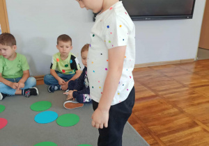 Chłopiec z grupy „Misie”skacze po kolorowych kropkach rozłożonych na dywanie.