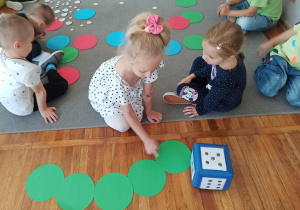 Dziewczynka liczy zielone kropki, zgodnie ze wskazaniem kropek znajdujących się na kostce do gry.