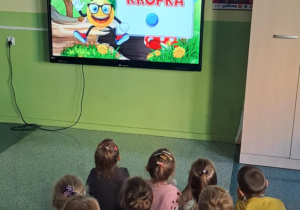 Dzieci siedzą na dywanie i oglądają film edukacyjny pt.: „Kropka”.