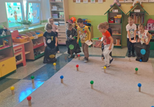 Dzieci zbierają piłki do worków na śmieci oznaczone kolorowymi kółkami.