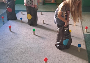 Dzieci zbierają piłki do worków na śmieci oznaczone kolorowymi kółkami.