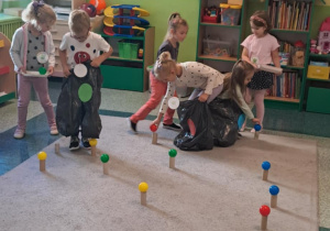 Dzieci zbierają piłki do worków na śmieci oznaczone kolorowymi kółkami.