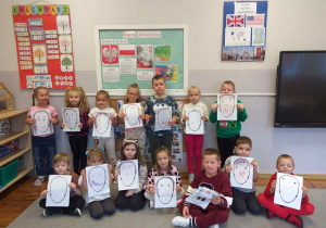 Dzieci z grupy Odkrywcy pozują do zdjęcia z wykonanym przez siebie swoimi podobiznami.