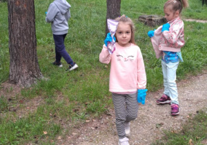 Dziewczynka trzyma śmieci w ręce reszta dzieci rozgląda się.