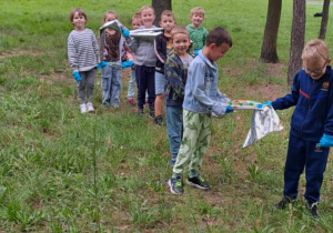 Dzieci stoją w zieleni i trzymają w rękach długą folię.