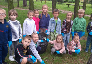 Grupowe zdjęcie na tle zieleni z workiem zebranych śmieci.