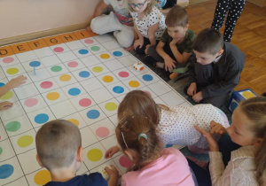 Na zdjęciu widać dzieci które bawią się na specjalnej macie do kodowania rozwiązując zadania związane z kropkami za pomocą robotów Zosia