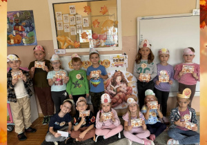 Na zdjęciu pozują dzieci z opaskami na głowie, przypiętymi orderami oraz dyplomami trzymanymi w rączkach