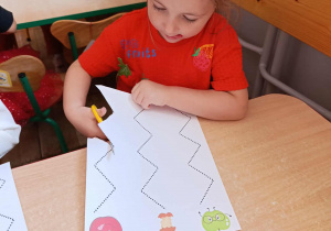 Dziewczynka wycina nożyczkami drogę do jabłka.