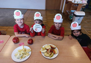 Dzieci w opaskach z jabłkami pozują do zdjęcia z jabłkami.