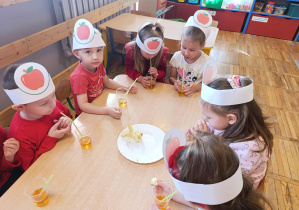 Dzieci piją sok jabłkowy z kubeczka przez słomkę.