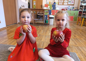 Dziewczynki ubrane na czerwono prezentują jabłka.