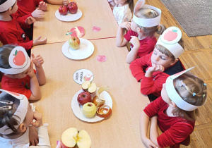 Dzieci siedzą przy wspólnym stole i słuchają o budowie jabłka oglądając owoc.