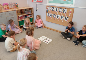 Na zdjęciu widzimy dziewczynkę gdy porównuje zbiory jabłek i je przelicza.