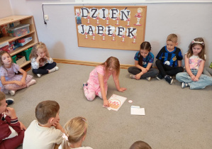 Dziewczynka z grupy Odkrywcy wkłada do koszyczka jabłka.