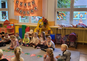 Dzieci siedzą na dywanie, dziewczynka liczy jabłka i dopasowuje do odpowiedniej cyfry na drzewie.