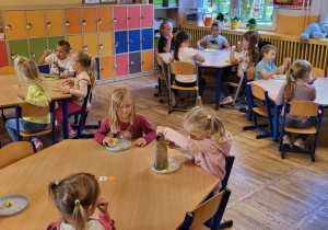 Dzieci siedzą przy stolikach, trą jabłka na tarce.