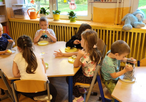 Dzieci siedzą przy stolikach, trą jabłka na tarce.