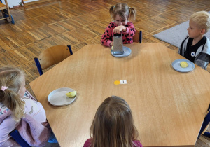 Dzieci siedzą przy stolikach, trą jabłka na tarce.