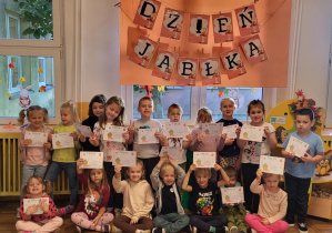 Dzieci pozują do wspólnego zdjęcia trzymając w ręku dyplomy z okazji Dnia Jabłka.