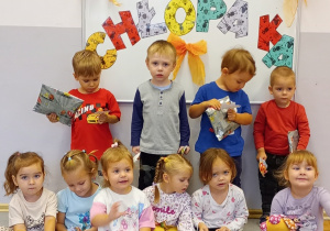 Dzieci z grupy Biedronki stoją i siedzą na tle tablicy z napisem Dzień Chłopaka.