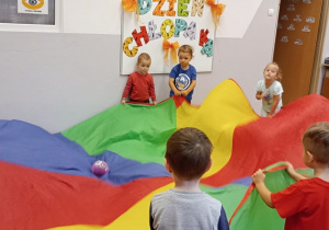 Przedszkolaki trzymają chustę animacyjną i przetaczają piłkę.